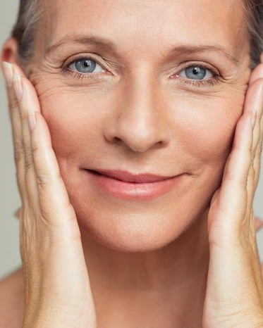 Mulher madura sorrindo, tocando o rosto com naturalidade e leveza